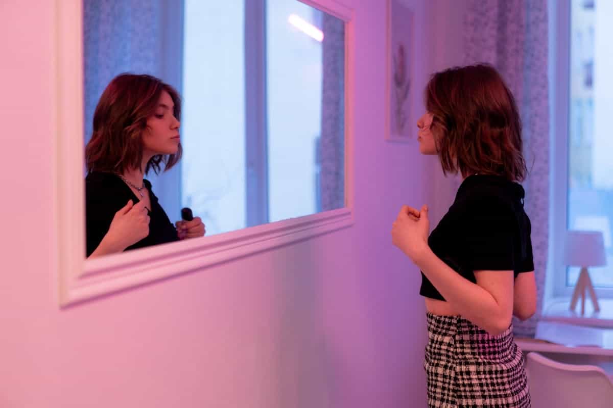 Brunette woman with a bob haircut gazing intently at her reflection in an indoor mirror in soft lighting representing the Jungian concept of shadow integration and honest self-confrontation in mirror dream psychology