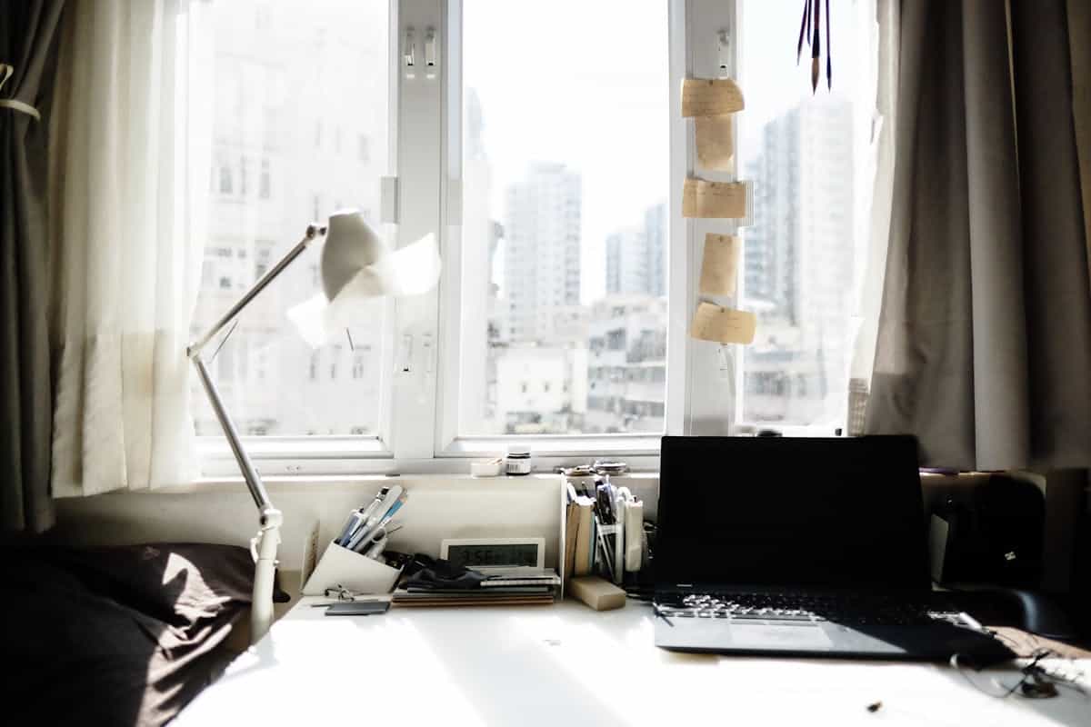 Bright home workspace with a laptop and lamp beside a large window, illustrating feng shui desk placement near a window