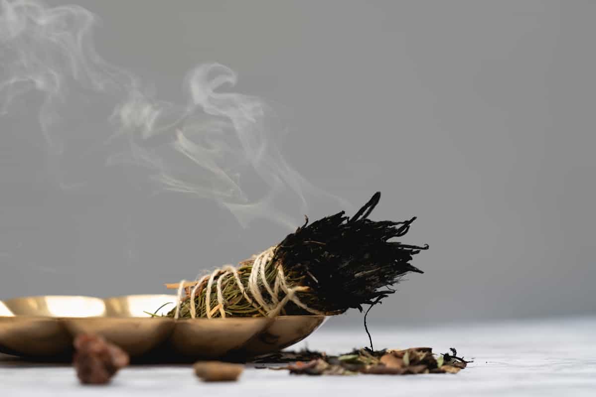 Bundle of white sage burning with fragrant smoke rising in a dimly lit indoor space for energy cleansing ritual