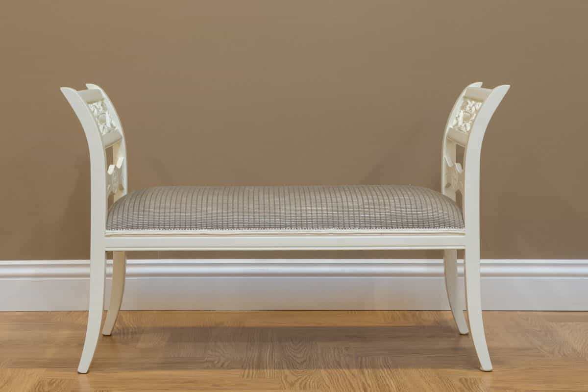 White entryway bench illustrating how to size and place a mirror above it Classic white wooden bench against a beige wall, showing how to size a mirror above an entryway bench