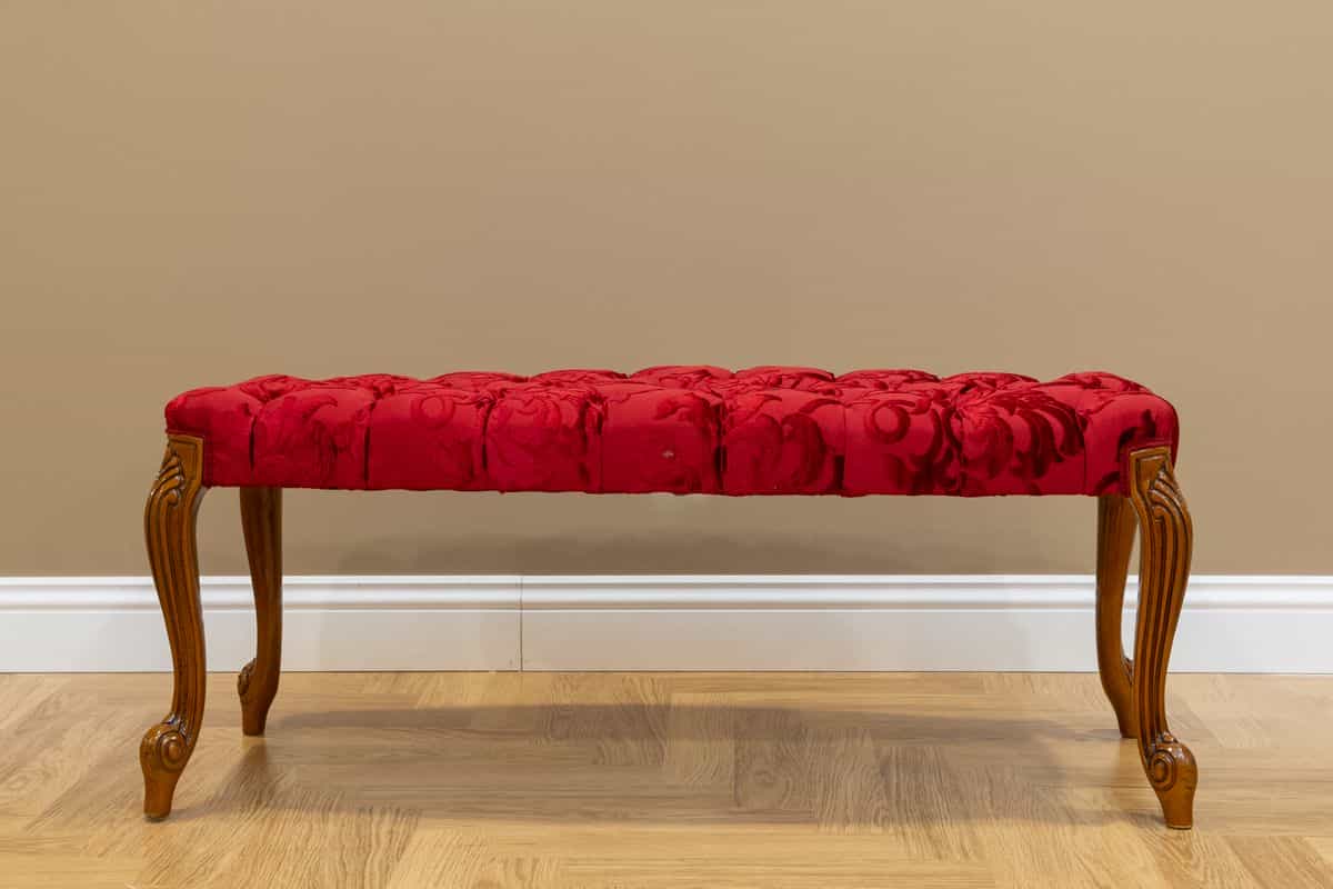 Upholstered bench illustrating a stylish entryway bench with mirror combo Luxurious red upholstered bench with wooden legs against a beige wall, showing a stylish entryway bench with mirror combo