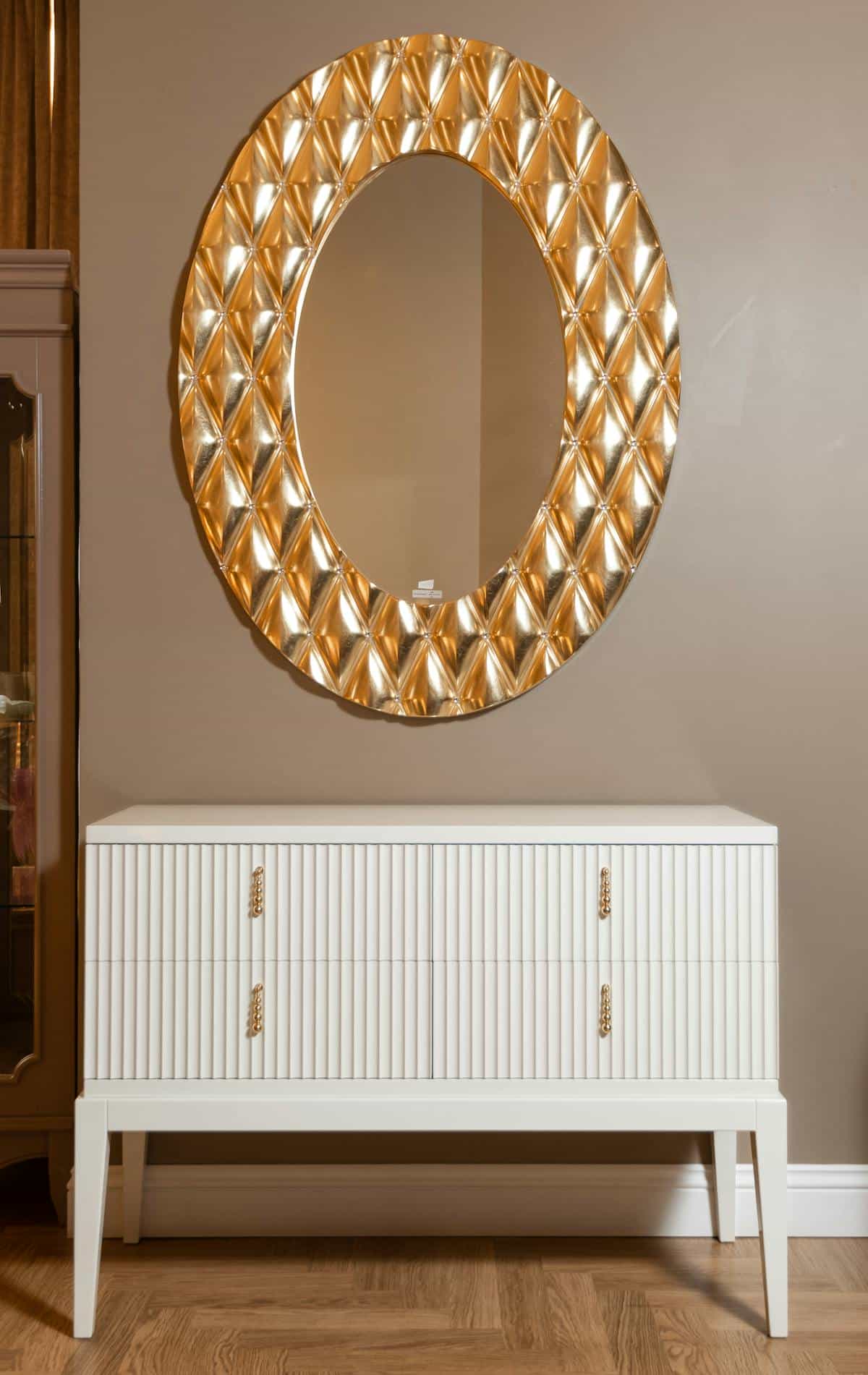 Elegant gold ornate mirror above a white cabinet in a styled neutral interior