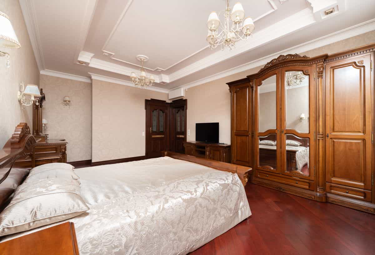 Luxurious bedroom with rich wooden furniture and chandelier lighting, illustrating wood mirror frame finishes