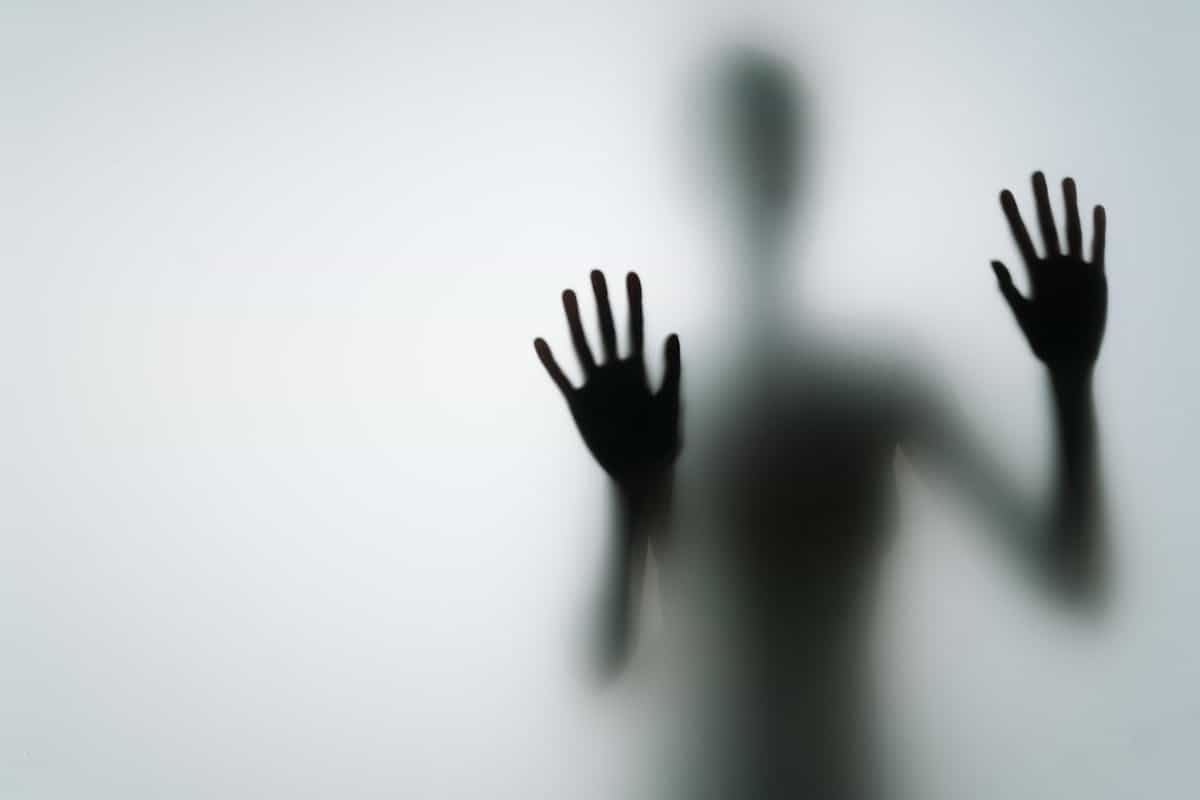 Abstract silhouette of a person pressing hands against glass in dim light representing the disturbing experience of finding no reflection at all in a mirror dream