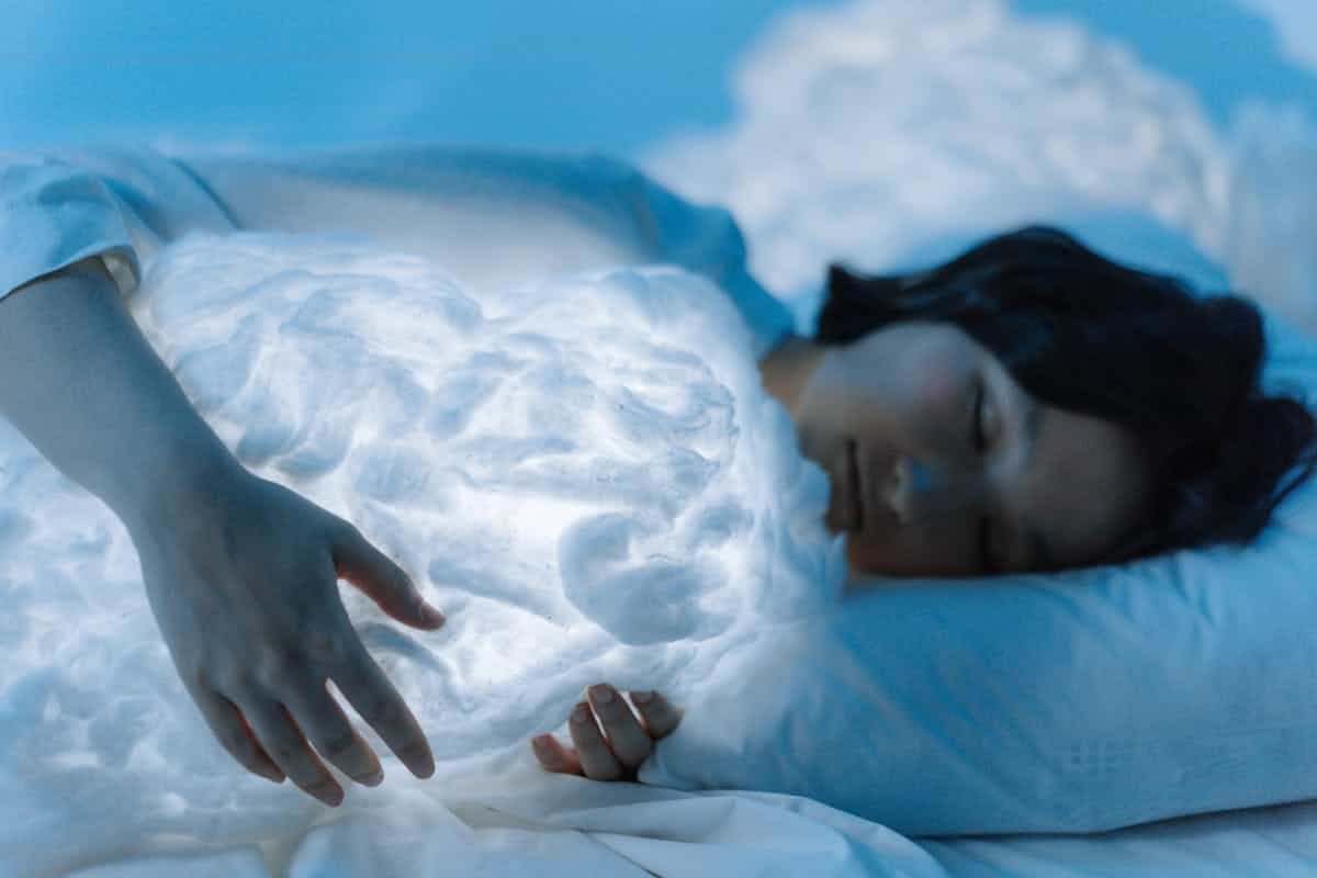 Peaceful image of a woman sleeping on a white pillow with soft blue light suggesting the practice of journaling and working with mirror dreams after waking