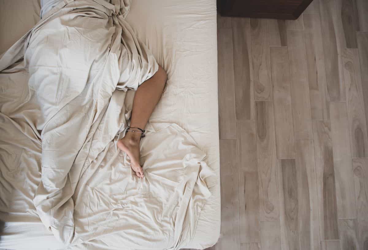 Overhead view of a sleeper illustrating which way the head should face in feng shui Person sleeping peacefully under white sheets seen from above, illustrating the feng shui sleeping direction question