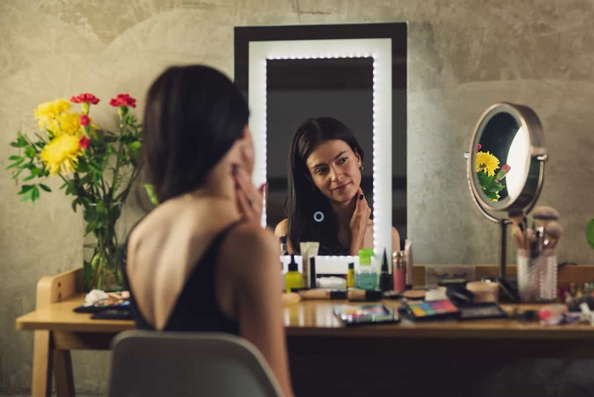 Makeup dressing-table vanity mirror in use illustrating a seated vanity mirror setup Woman sitting at a vanity applying makeup before a lit mirror, illustrating a makeup dressing-table vanity mirror