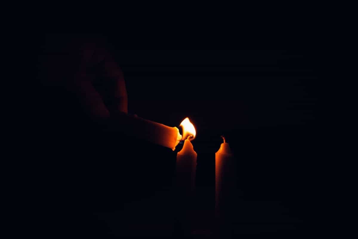 A hand lighting candles in a moody dark scene representing the dimly lit conditions deliberately used in scrying to induce the alpha-wave brain state associated with visionary perception
