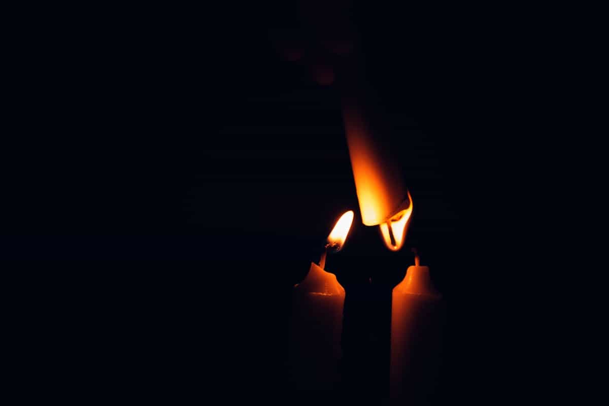 Lit candle flame burning clearly against a dark blurred background with warm orange glow and smoke rising