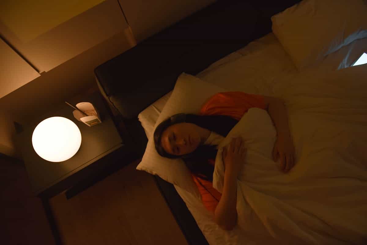 An Asian woman lies awake in bed under dim lighting at night, evoking the folk tradition of mirror dreams as significant spiritual omens