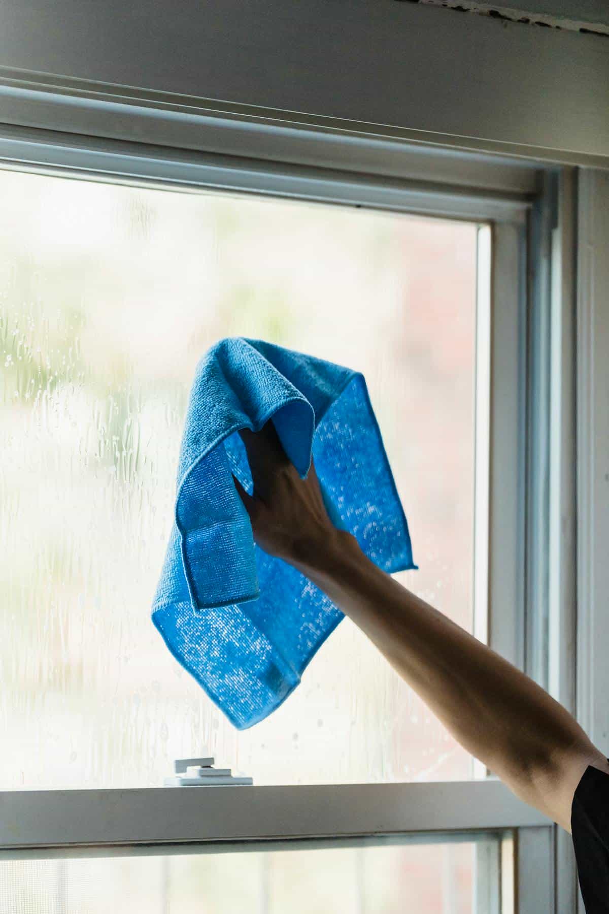 Close-up hand wiping glass mirror surface with cloth for streak-free cleaning
