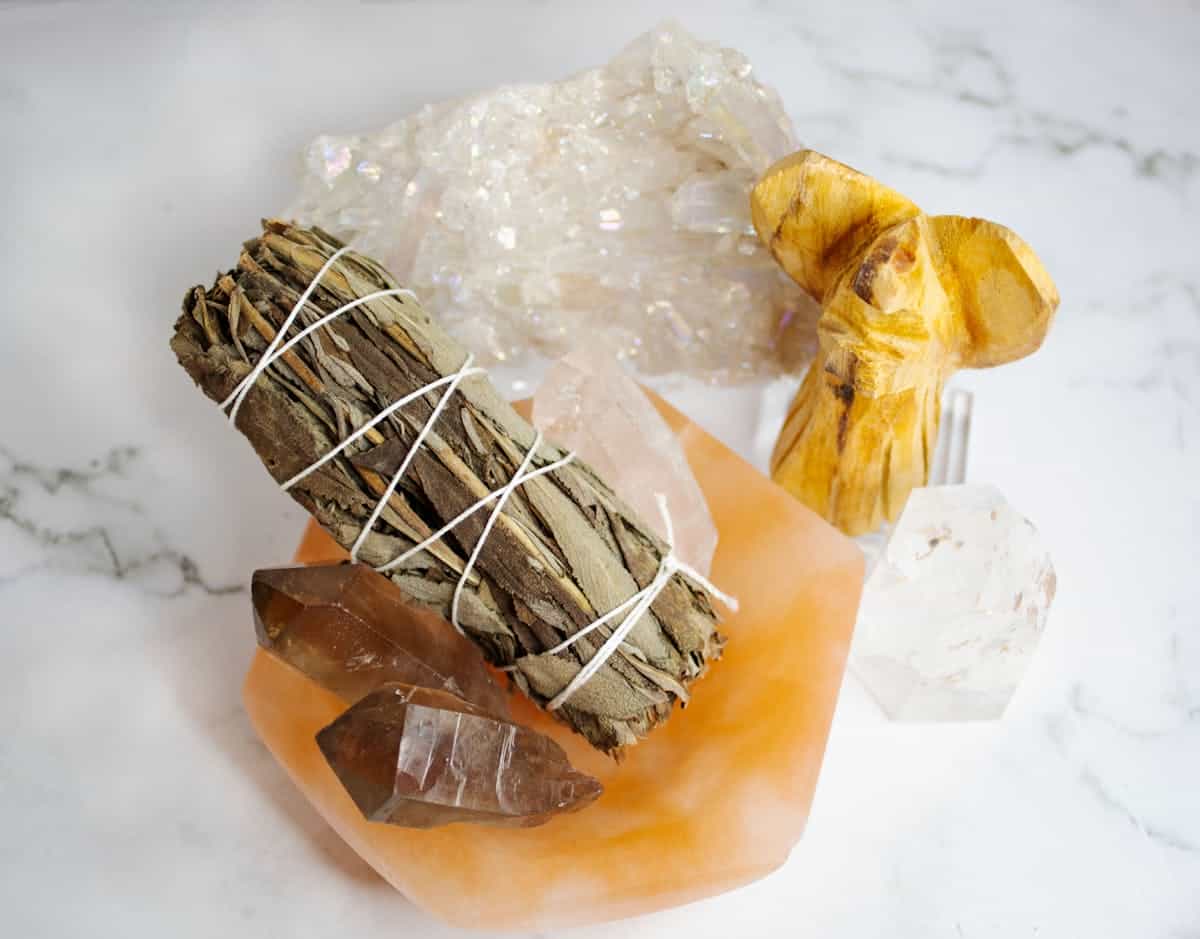 A still life of healing crystals a sage smudge stick and spiritual items on a marble surface representing the cleansing tools and intentional practice used after breaking a mirror