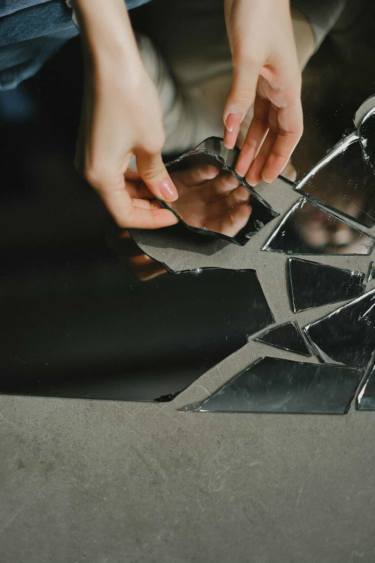 Hands among mirror shards on floor symbolising spiritual introspection after broken mirror dreams Hands touching reflective mirror shards on the floor symbolising introspection after a broken mirror dream