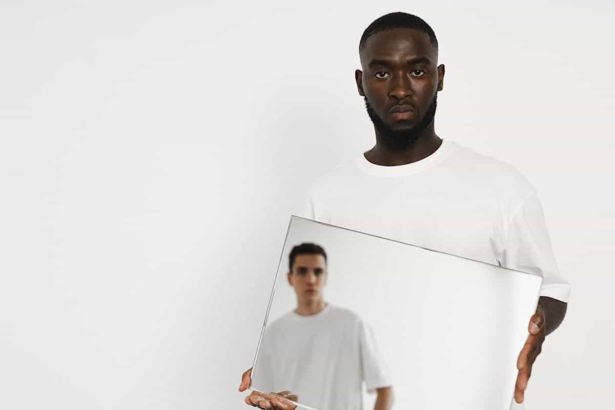 A man holding a mirror reflecting another person evoking the relational reading of cracked mirror dream meaning and how other people's actions affect self-image