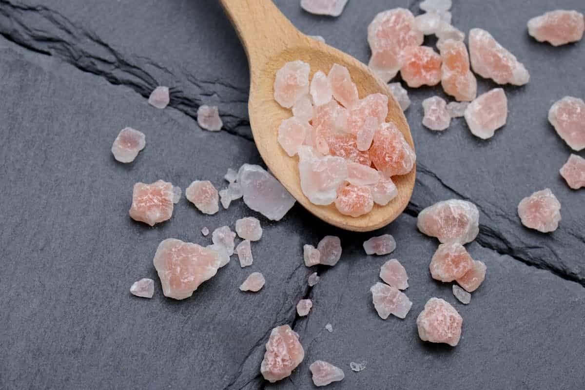 Pink Himalayan salt crystals on a wooden spoon against slate suggesting folk cleansing symbolism rather than chemistry